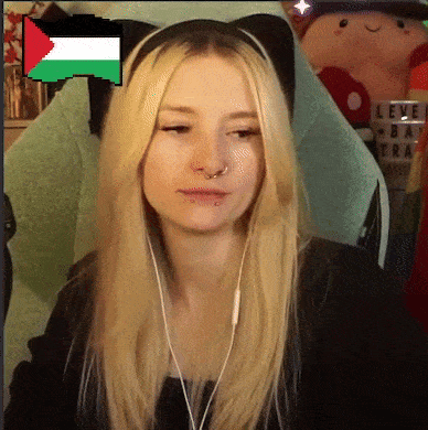 a blonde woman wearing headphones and a cat ear headband with a pixelated flag in the background