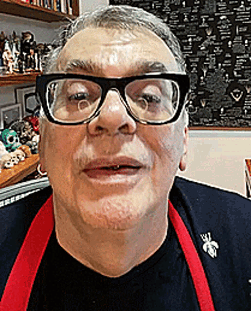 a man wearing glasses and a red apron is smiling