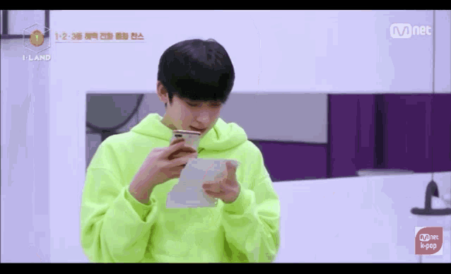 a young man in a neon green hoodie is holding a cell phone and a piece of paper .