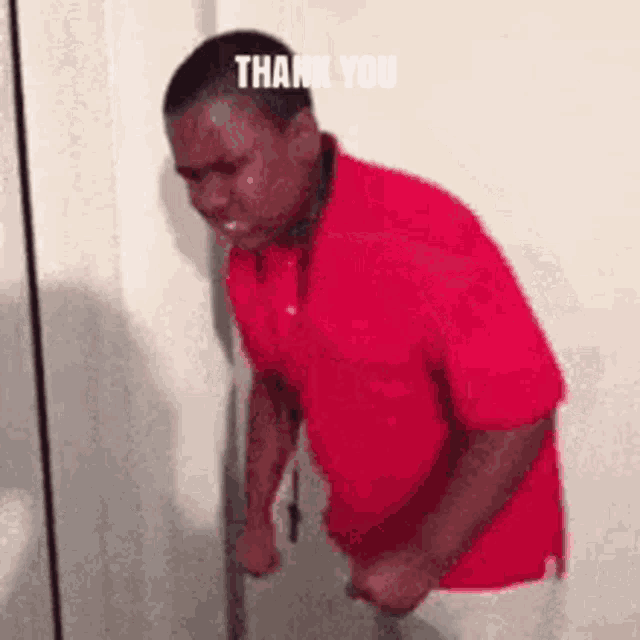 a man in a red shirt is crying while leaning against a wall and saying thank you .