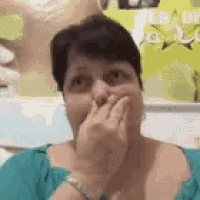 a woman in a blue shirt is covering her mouth with her hand .