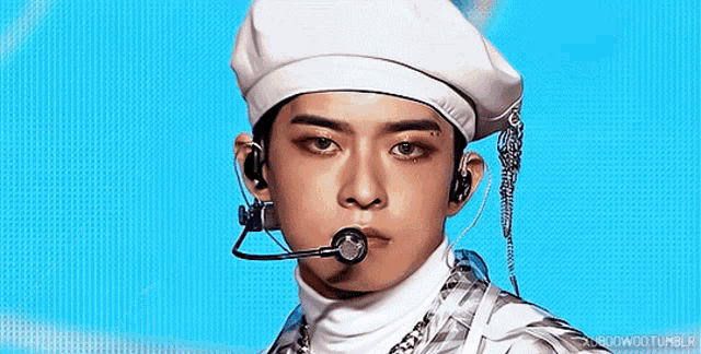 a young man wearing a white beret and a microphone looks at the camera
