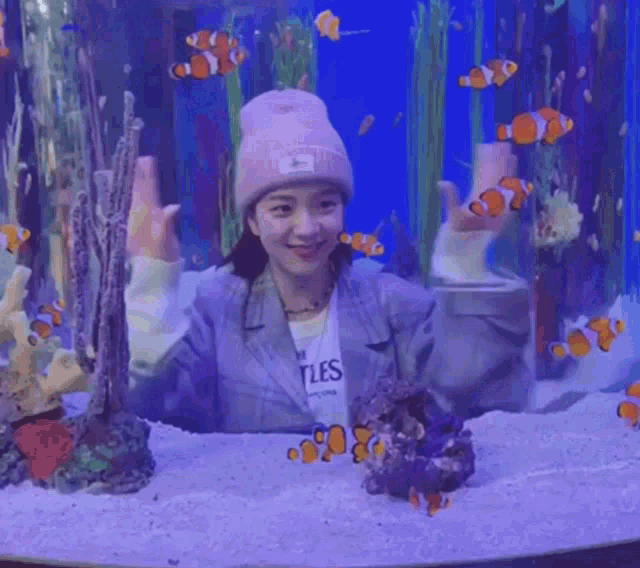 a woman in a pink hat is standing in front of an aquarium filled with fish .