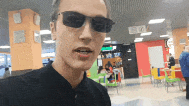 a man wearing sunglasses stands in a restaurant with a sign that says no smoking
