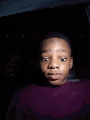a close up of a person 's face in the dark with a purple shirt on