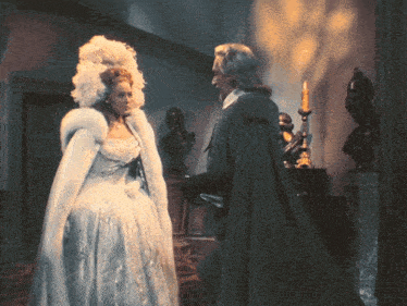 a woman in a white dress is standing next to a man in a black coat