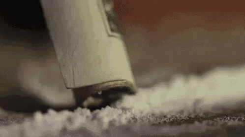 a close up of a dollar bill being used to snort cocaine on a table .