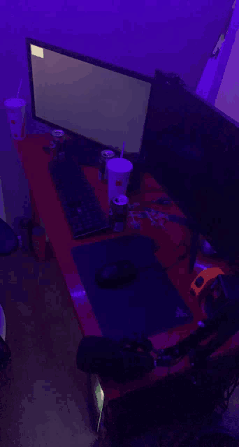 a computer desk with two monitors a keyboard and two cups of soda