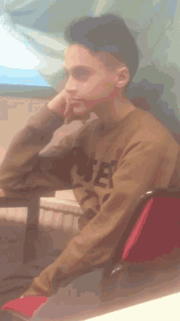 a boy wearing a sweatshirt that says " rite " sits at a table with his hand on his chin