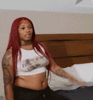 a woman with red hair is sitting on a bed wearing a crop top .