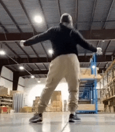 a man is dancing in a large warehouse with his arms outstretched .