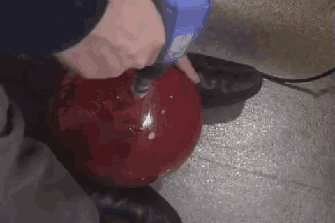 a person is holding a red bowling ball with a drill .