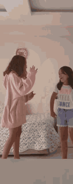 two young girls are dancing in a bedroom in front of a mirror .