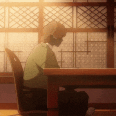 a man in a green shirt sits at a wooden table in front of a window