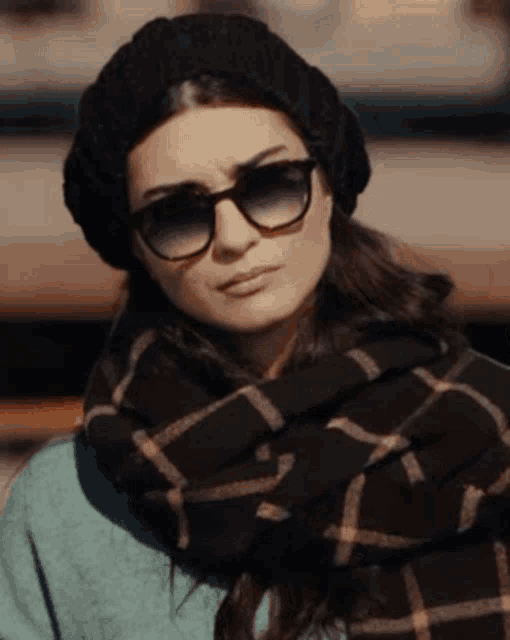 a woman wearing sunglasses and a scarf looks serious