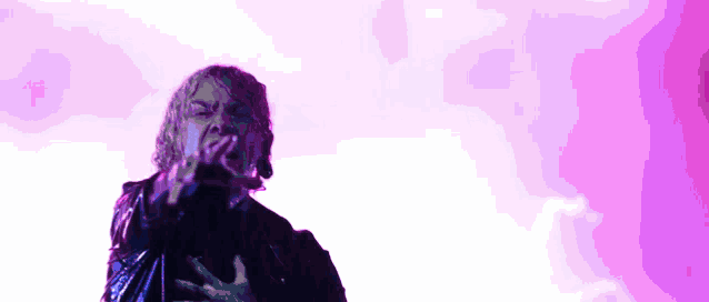 a man in a black jacket is singing into a microphone in front of a purple background