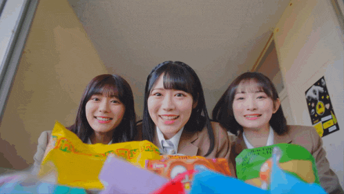 three girls are smiling while holding bags of snacks one of which has a sticker that says ' a ' on it