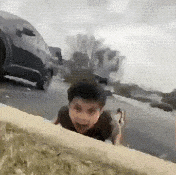 a young boy is crawling on the side of a road in front of a car .