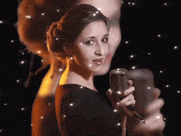 a woman singing into a microphone with a reflection of a man in the background