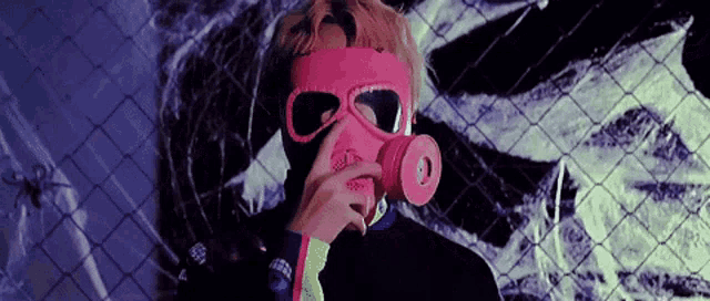 a man wearing a pink gas mask and sunglasses is standing next to a chain link fence .