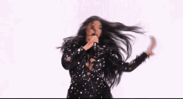 a woman in a black dress is singing into a microphone with her hair blowing in the wind .