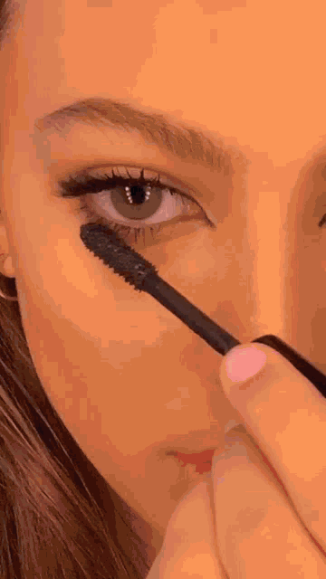 a close up of a woman applying mascara on her eye