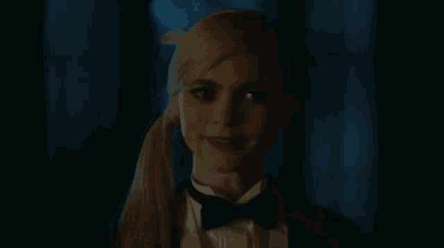 a close up of a woman wearing a tuxedo and bow tie in a dark room .