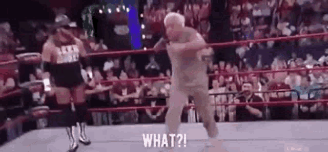 an elderly man is dancing in a wrestling ring while a wrestler watches .