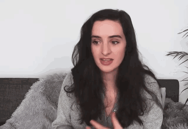 a woman with long dark hair is sitting on a couch with a fluffy blanket .