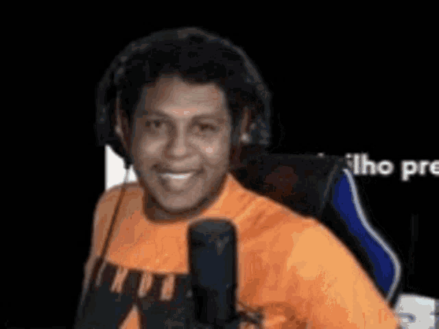 a man wearing headphones and an orange shirt is sitting in a chair in front of a microphone .