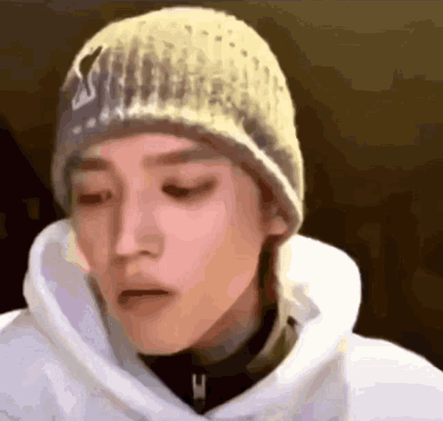 a man wearing a white hoodie and a yellow beanie is making a funny face .