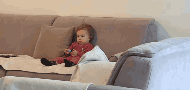 a baby is sitting on a couch with a remote control in his hand