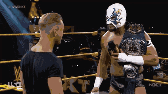 a wrestler in a mask talks to a man in a black shirt