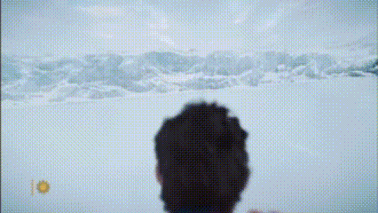 a man in a red cape is standing in the snow looking at a mountain .