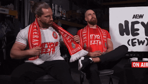 two men are sitting in front of an aew sign