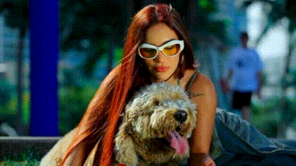 a woman with red hair and sunglasses is holding a small dog .