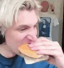 a man in a blue shirt is eating a hamburger in front of a mona lisa painting .