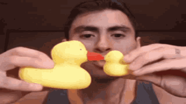 a man is holding two yellow rubber ducks in front of his mouth
