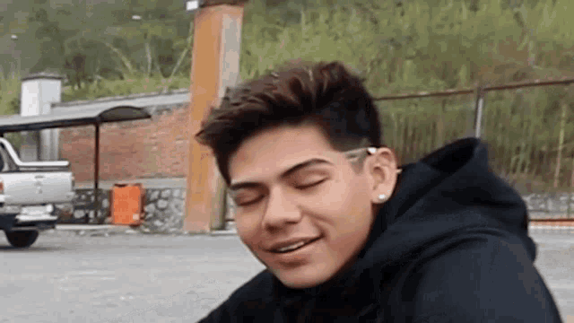 a young man in a black hoodie is smiling with his eyes closed .