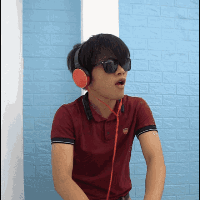 a young man wearing sunglasses and headphones stands in front of a blue wall