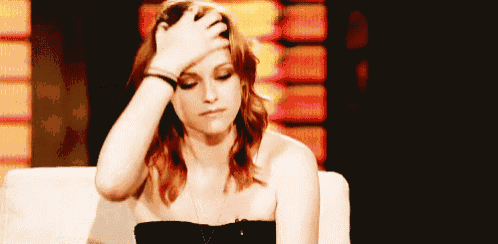 a woman is sitting on a couch holding her head with her hand