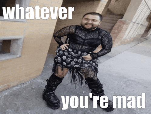 a man in a lace dress and boots is standing in front of a brick building and says whatever you 're mad