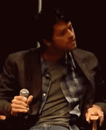 a man in a suit is holding a microphone while sitting in a chair