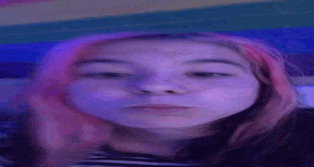 a girl with pink hair is taking a selfie in a dark room with purple lights .
