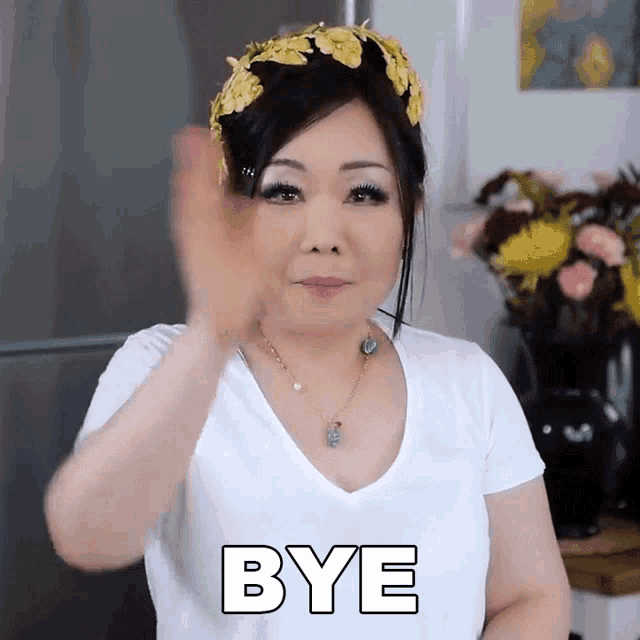 a woman wearing a flower crown waves her hand in front of the word bye