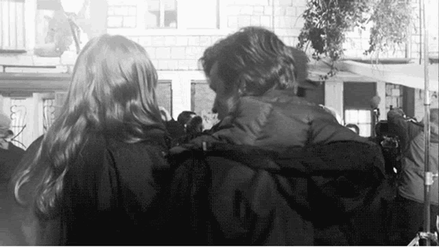a black and white photo of a man and woman hugging each other .