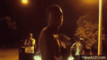 a group of people are dancing in front of a car at night on make a gif