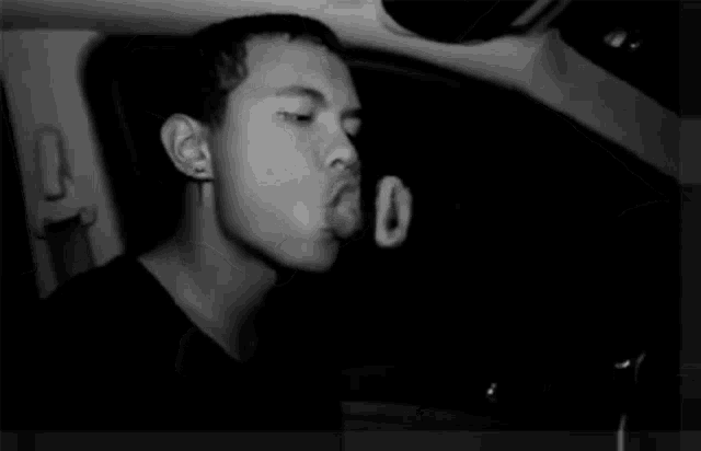 a black and white photo of a man blowing bubbles in a car