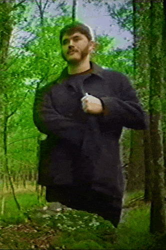 a man in a black jacket is standing in a forest