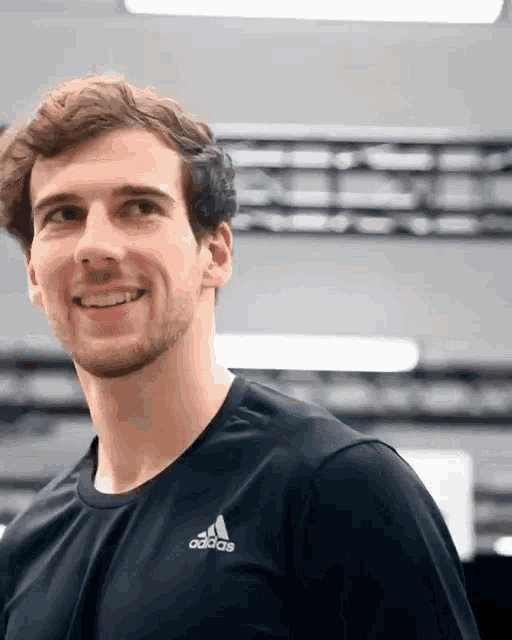 a man wearing an adidas shirt is smiling